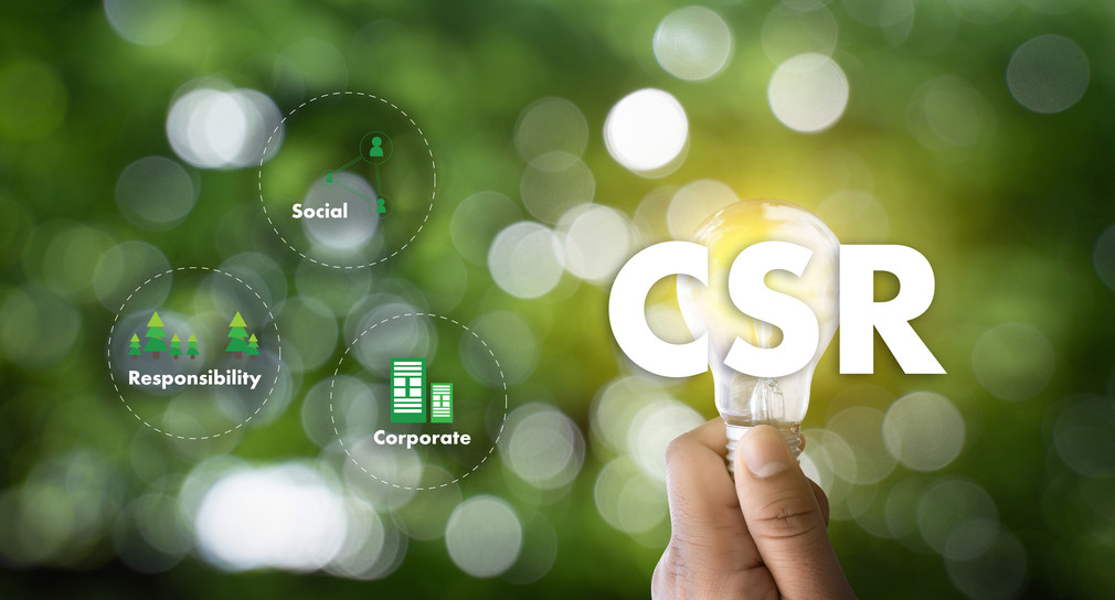 Symbolbild für Corporate Social Responsibility (CSR): Grüner Hintergrund, Hand die eine Glühbirne hält, die Buchstaben CSR und Symbole für Verantwortung, Unternehmen und Soziales.