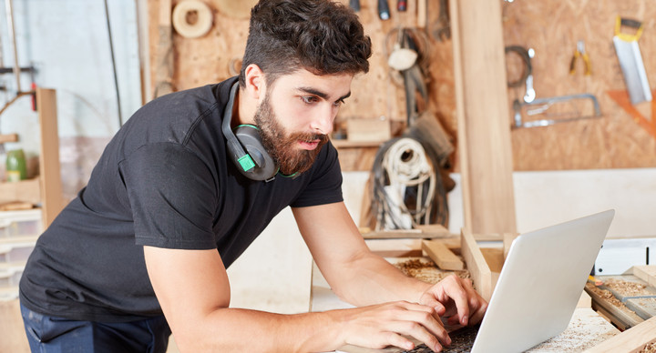 Junger Mann am Laptop in einem Handwerksbetrieb