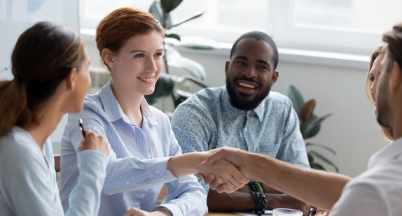 Ein Mann und eine Frau geben sich in einem Meeting mit anderen die Hand