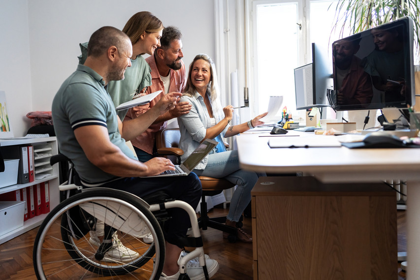 Gruppe von Büromitarbeitenden, ein Mann sitzt im Rollstuhl