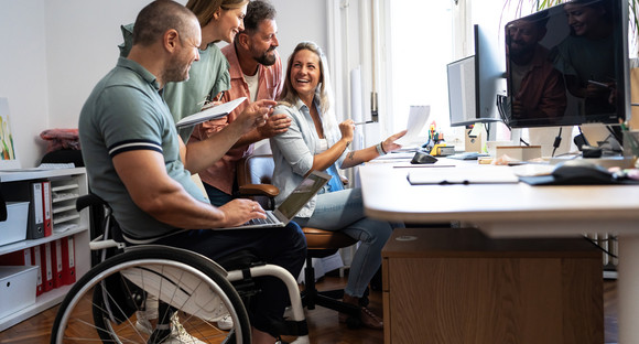 Gruppe von Büromitarbeitenden, ein Mann sitzt im Rollstuhl