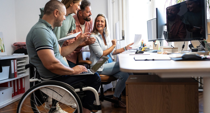 Gruppe von Büromitarbeitenden, ein Mann sitzt im Rollstuhl