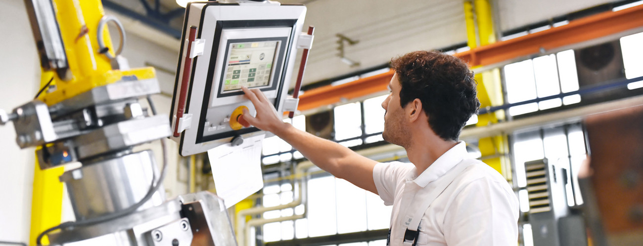 Junger Maschinenbauer steuert eine Maschine über einen Monitor (Bild: © industrieblick, stock.adobe)