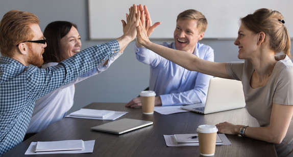 Zwei Frauen und zwei Männer schlagen in einem Meeting die Hände zusammen