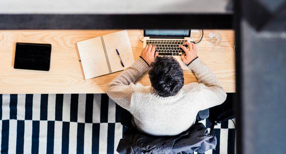 Junger Mann sitzt an einen Laptop