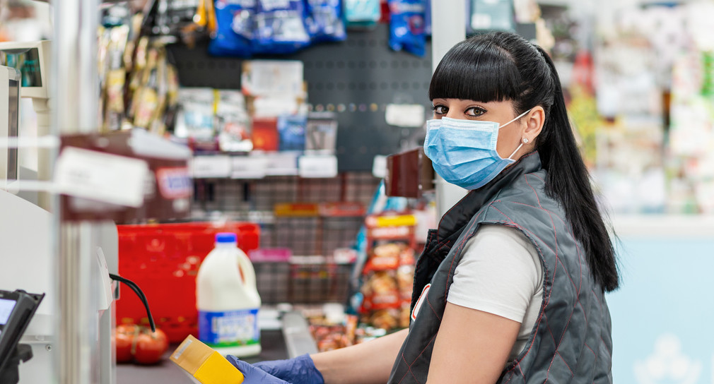 Kassiererin mit Mundschutz an einer Supermarktkasse
