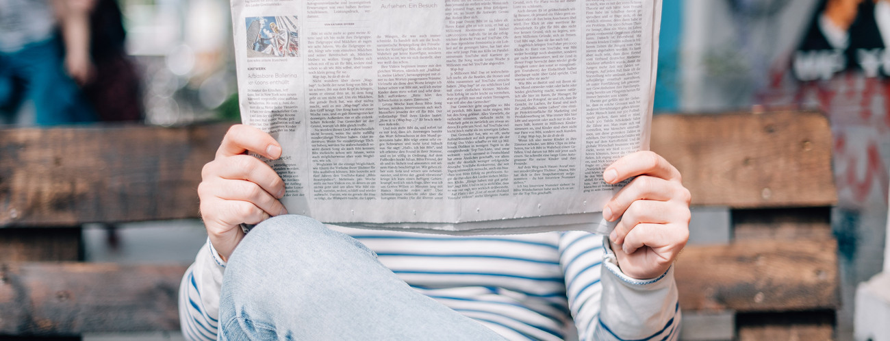 Frau sitzt auf einer Bank und liest eine Zeitung (Bild: © Roman Kraft / Unsplash)