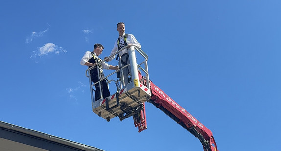 Staatssekretär Thomas Dörflinger steht auf einem Kran udn wird in die Luft gehoben. Der Himmel ist blau.