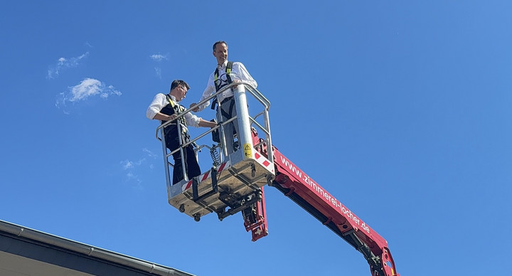 Staatssekretär Thomas Dörflinger steht auf einem Kran udn wird in die Luft gehoben. Der Himmel ist blau.