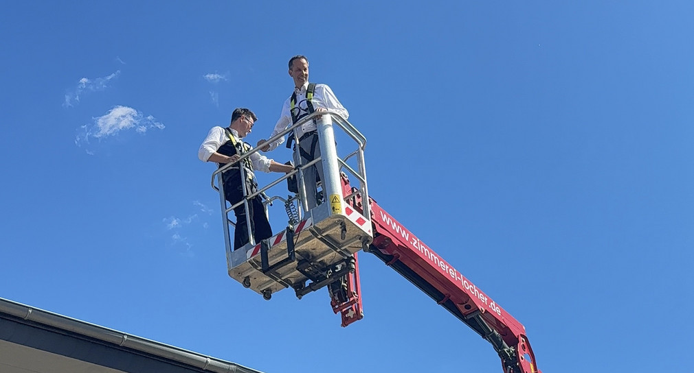 Staatssekretär Thomas Dörflinger steht auf einem Kran udn wird in die Luft gehoben. Der Himmel ist blau.