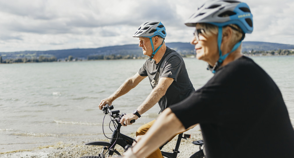 Zwei Rentner stehen mit ihren Fahrrädern am Bodensee und schauen auf den See.