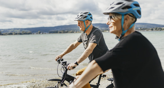 Zwei Rentner stehen mit ihren Fahrrädern am Bodensee und schauen auf den See.