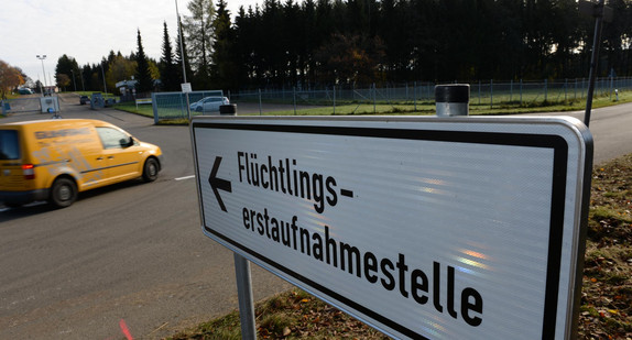 Ein Schild mit der Aufschrift „Flüchtlingserstaufnahmestelle“, im Hintergrund ein Fahrzeug an einer Einfahrt.