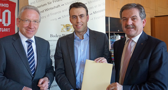 Finanz- und Wirtschaftsminister Nils Schmid übergibt einen Förderbescheid an Klaus Moser, Hauptgeschäftsführer (links) und Carl Trinkl, Präsident der IHK Ostwürttemberg.