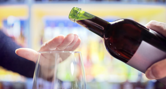 Eine Hand will Rotwein in ein Glas gießen, eine andere Hand verweigert dies.