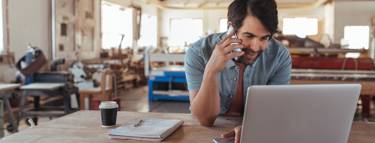 Ein Handwerker schaut auf sein Laptop und telefoniert mit seinem Smartphone (Bild: © mavoimages, stock.adobe)