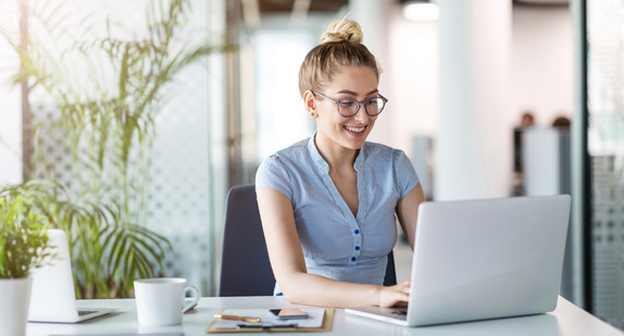 Junge Frau sitzt in einem Büro vor einem Laptop