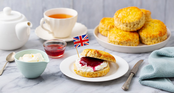 Scones, tea cakes with jam, clotted cream with the flag of Great Britain. Traditional British teatime. Grey background.