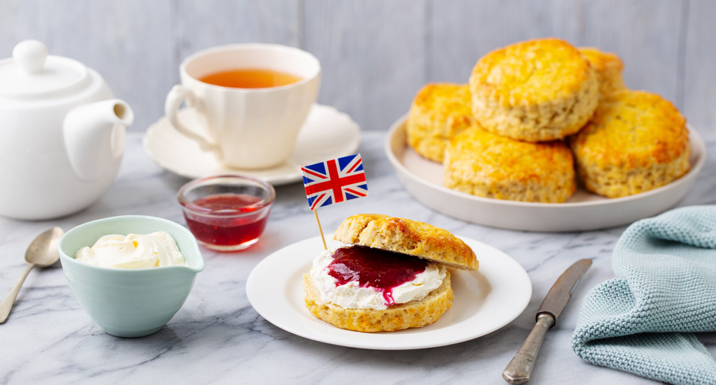 Scones, tea cakes with jam, clotted cream with the flag of Great Britain. Traditional British teatime. Grey background.