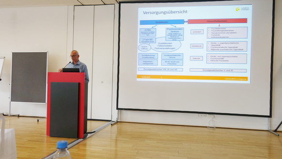 Fachtag Versorgung von traumatisierten Geflüchteten Michael Köber, Landratsamt Esslingen, spricht vor Publikum in Veranstaltungssaal