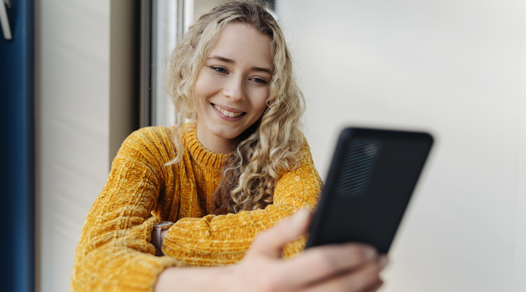Junge blonde Frau mit Handy in der Hand.