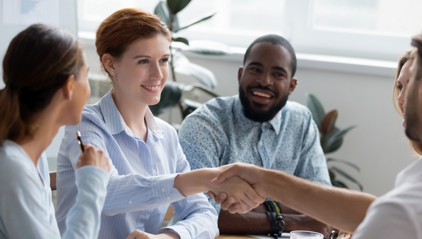 Ein Mann und eine Frau geben sich in einem Meeting mit anderen die Hand