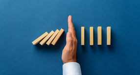 Eine Hand verhindert, dass alle Dominosteine umfallen.