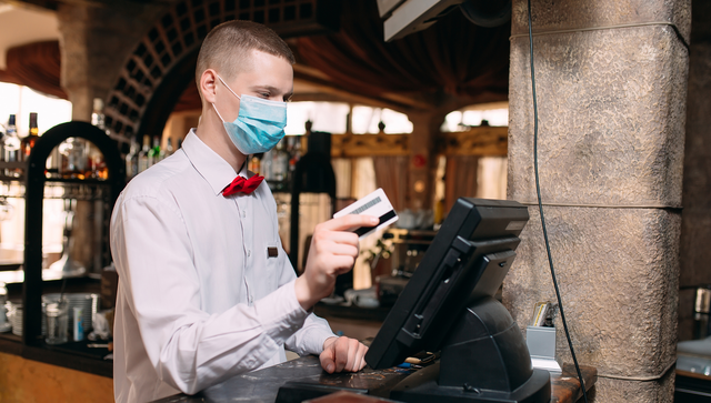 Ein junger Kellner bucht den Rechnungsbetrag &uuml;ber eine Kreditkarte