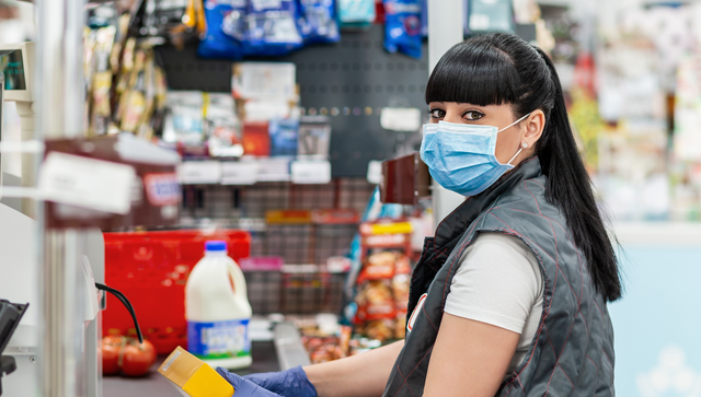 Kassiererin mit Mundschutz an einer Supermarktkasse