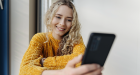 Junge blonde Frau mit Handy in der Hand.