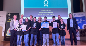 Eine Gruppe von Sch&uuml;lern auf einer B&uuml;hne. Einige Kinder halten eine Urkunde nach oben.
