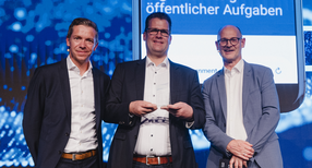 Drei M&auml;nner auf eine B&uuml;hne mit dem Preis in den H&auml;nden.